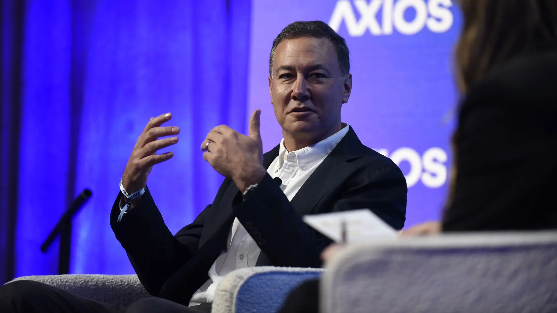 Yahoo CEO Jim Lanzone in a dark suit and white shirt gestures while speaking on a panel; a blue backdrop with the Axios logo is visible behind him.