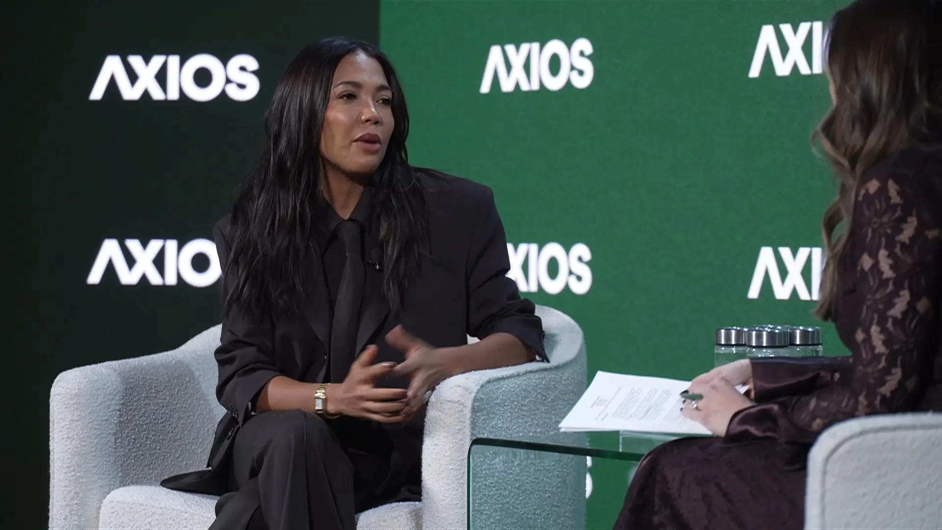 Grede wearing a full black outfit in front of an Axios banner