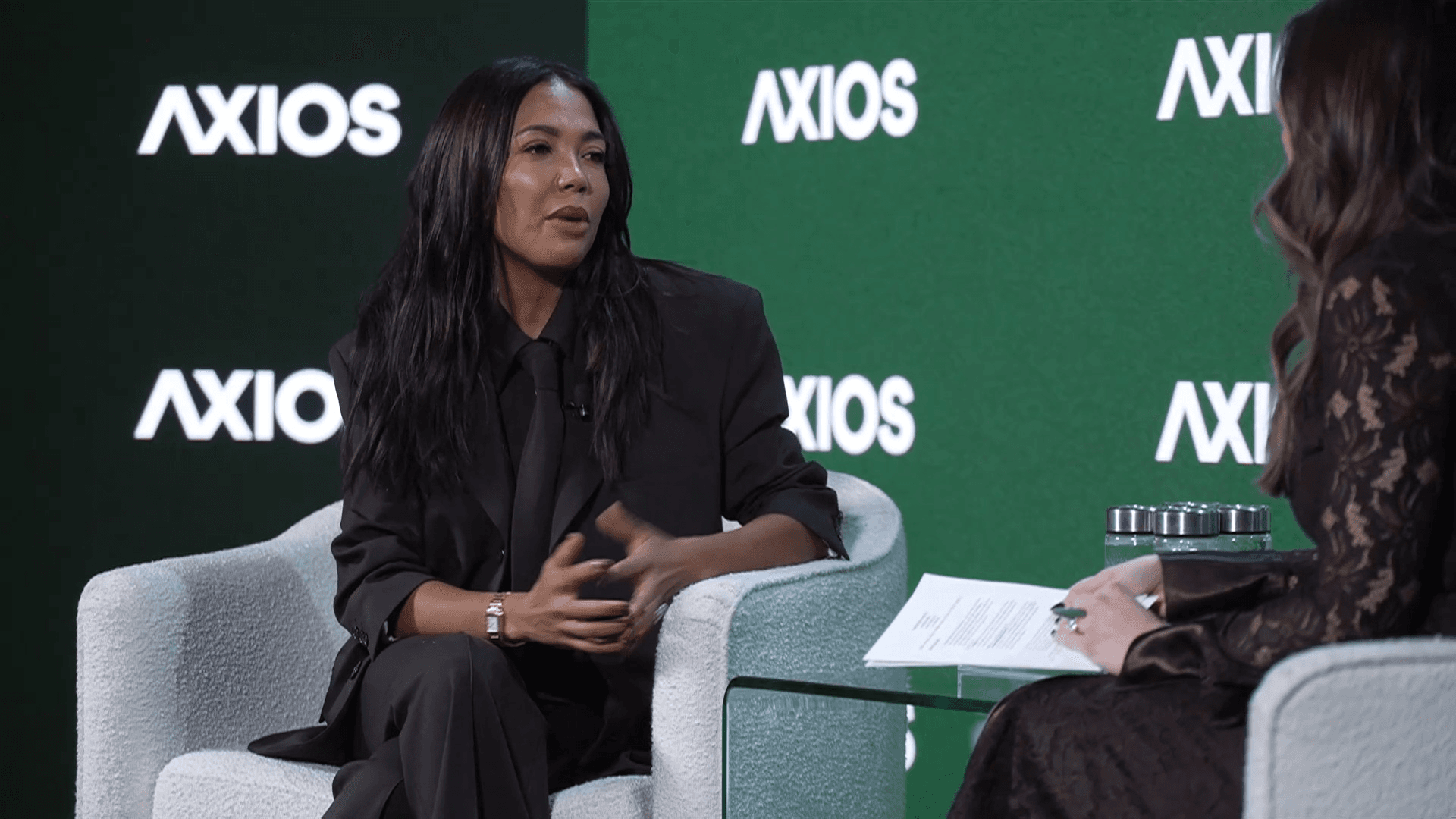Grede wearing a full black outfit in front of an Axios banner